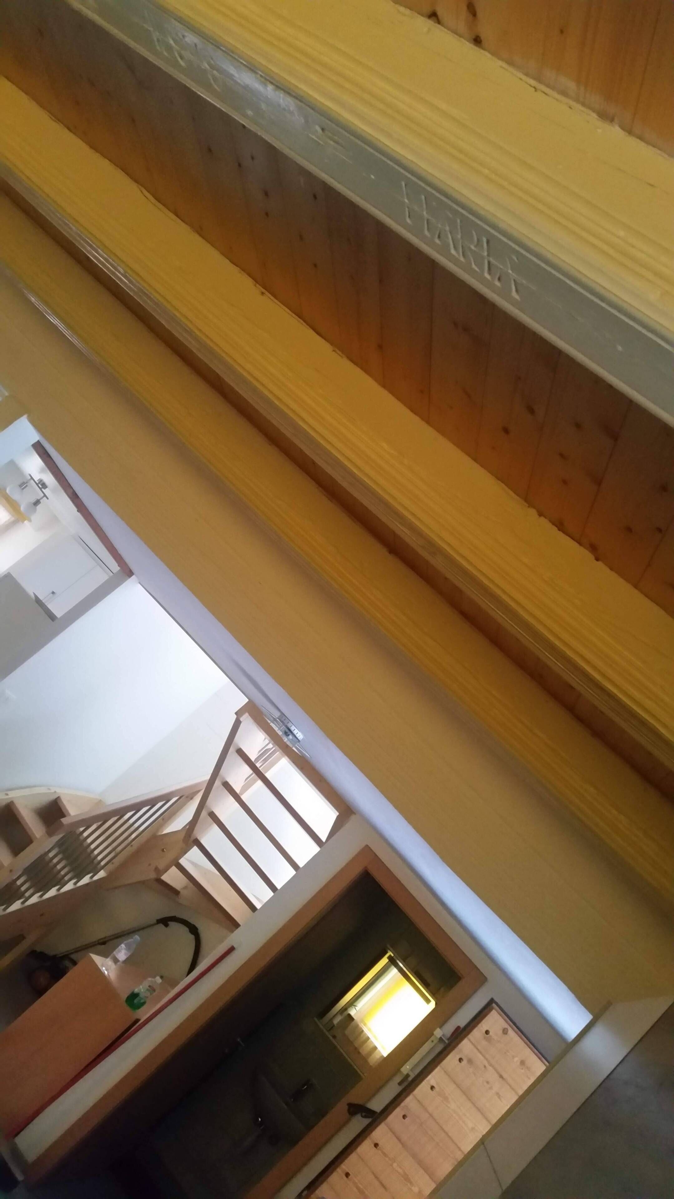 Una habitación con techo de madera, escalera a la vista y una ventana con luz natural.