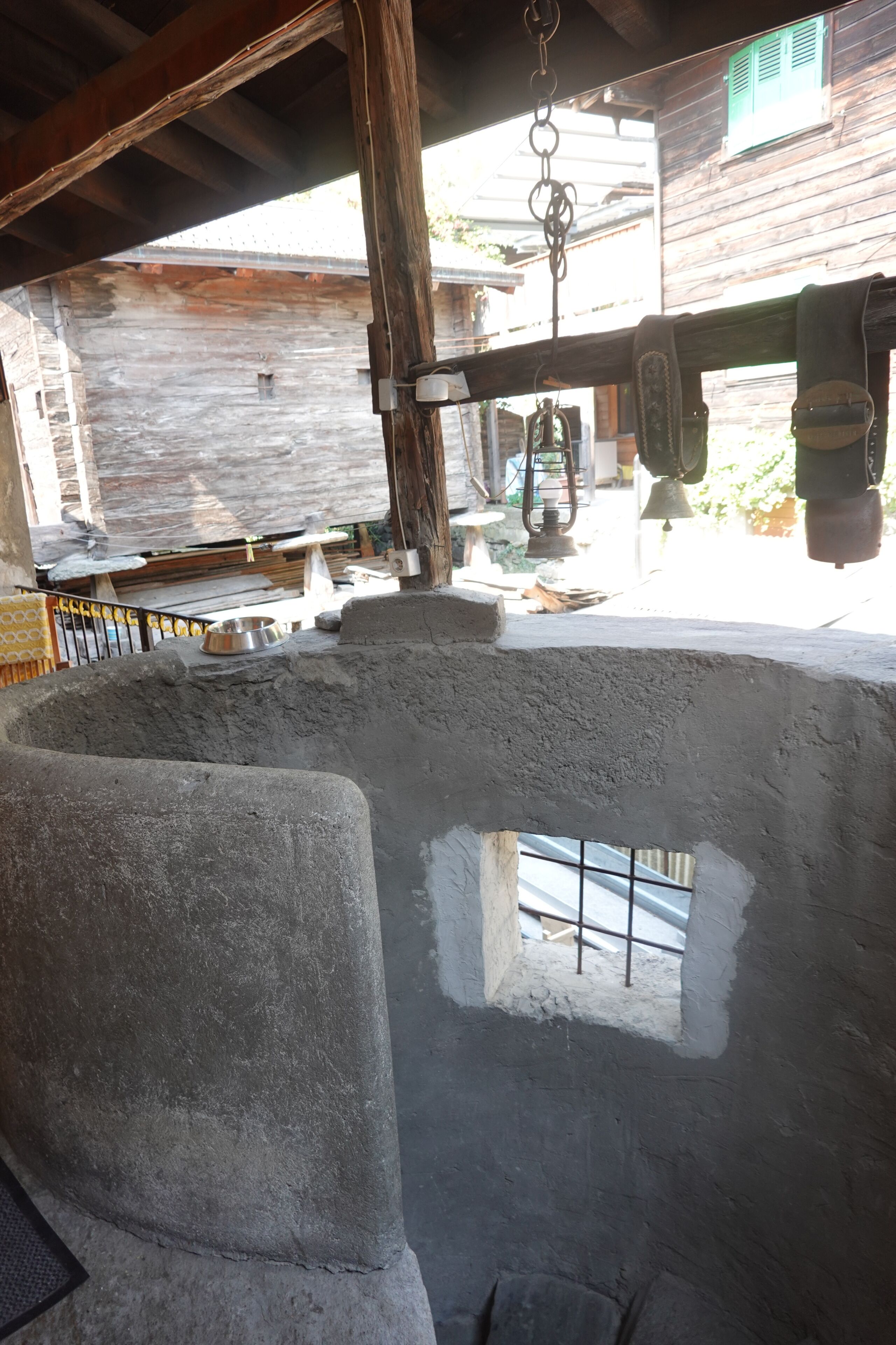 A rustic outdoor area with a concrete structure, wooden beams, and a metal bell.