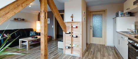 Una cocina moderna con suelo de madera, una estantería empotrada para vinos y una zona de comedor con mesa y sillas de madera.