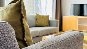 Ein modernes Wohnzimmer mit einem grauen Sofa, einem grünen Kissen und einem Flachbildfernseher auf einem Holzboden.