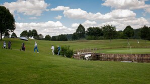 Ein Golfplatz mit einer Steinsbrücke über einem Teich, üppigem Grün und blauem Himmel.