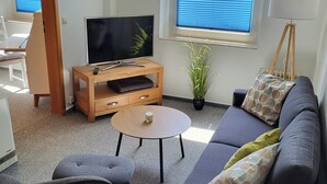 A living room with a sofa, armchair, coffee table, TV, and a potted plant. - Vacation apartment "Kormoran" (Kargow)