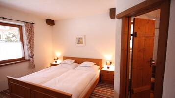 Una cama doble con dos mesitas de noche, una ventana con cortinas, un cuadro enmarcado en la pared y una puerta de madera.