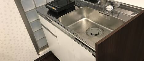 A kitchen with a stainless steel sink, a black induction cooktop, and white cabinets.