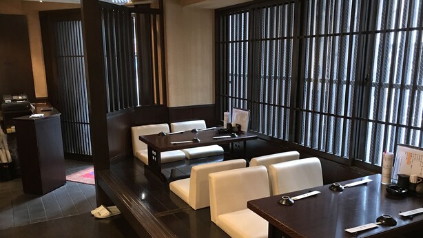 A modern restaurant with dark wood furniture, white cushioned seating, and a large window with vertical blinds. - HOTEL OWL Tokyo (Tokyo)