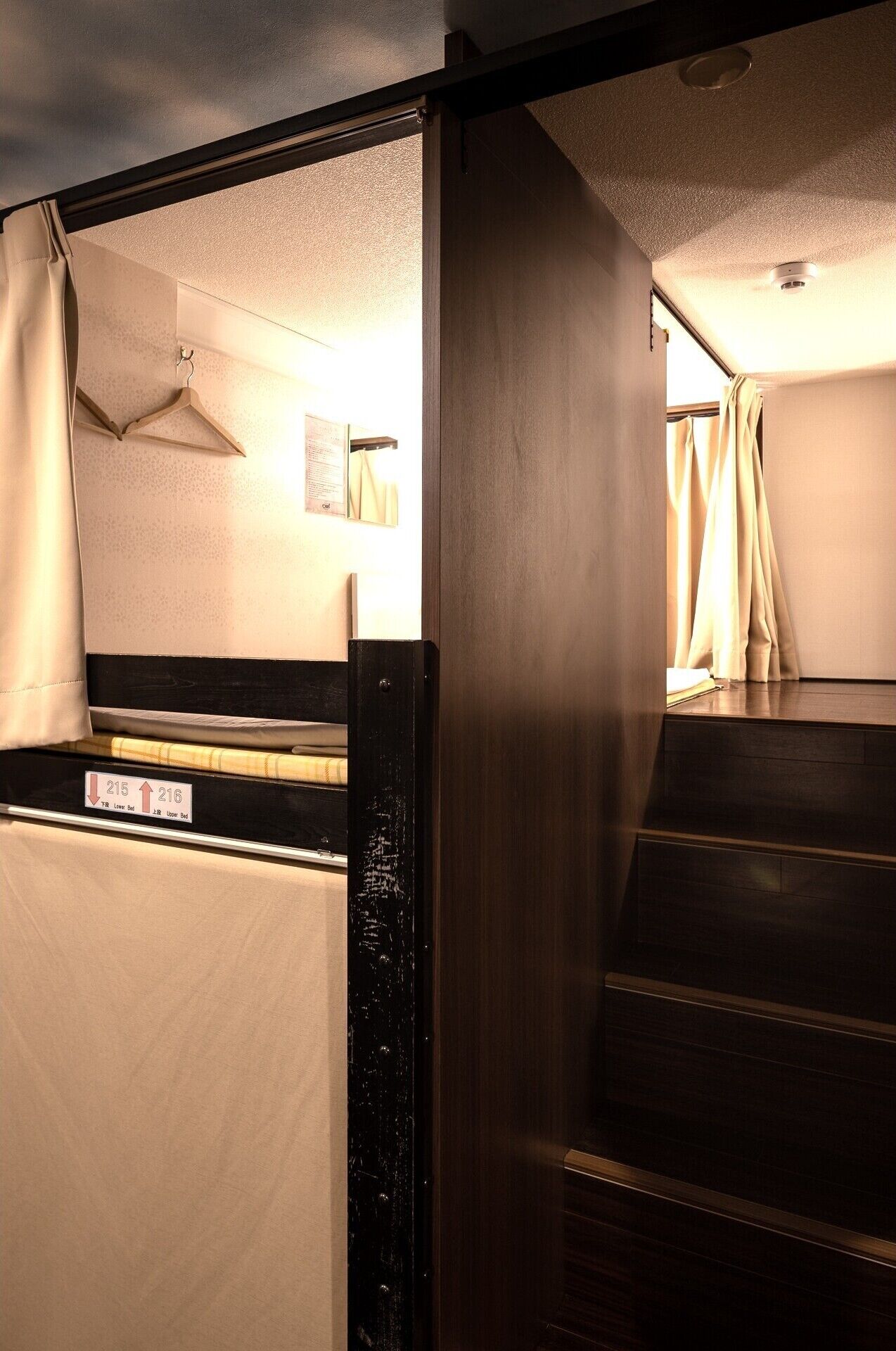 Une chambre d’hôtel avec un lit, une petite table, une lampe fixée au mur et une fenêtre avec des rideaux.