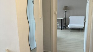 Un couloir avec une porte blanche donnant sur une pièce où se trouvent un lit et une lampe.