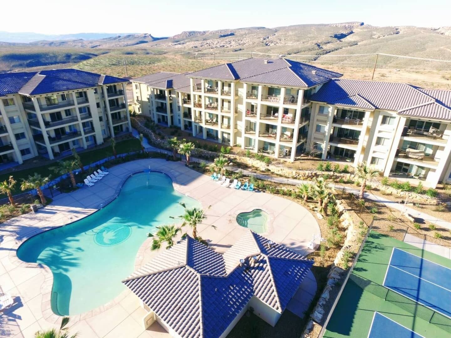 A resort with a swimming pool, tennis courts, and multiple-story buildings with balconies.