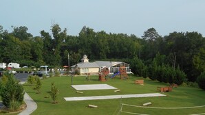 Une zone herbeuse avec des jeux pour enfants, un bâtiment doté d’un toit en pente et un parking où sont stationnés des véhicules récréatifs.
