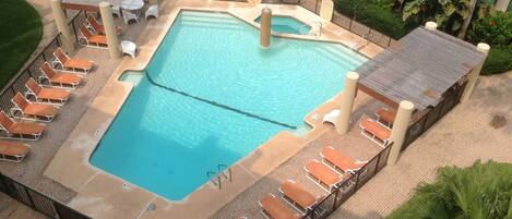 A rectangular swimming pool with a diving board, surrounded by lounge chairs and a fence.