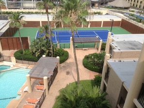 Un espace piscine aménagé sur le toit, avec un court de tennis, des palmiers et un petit jardin.