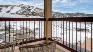 A balcony with a view of a snowy mountain landscape, a metal table, and a wicker chair. - True Ski-in Ski-Out Luxury 3bd with Huge views from 5th floor end unit (Steamboat Springs)