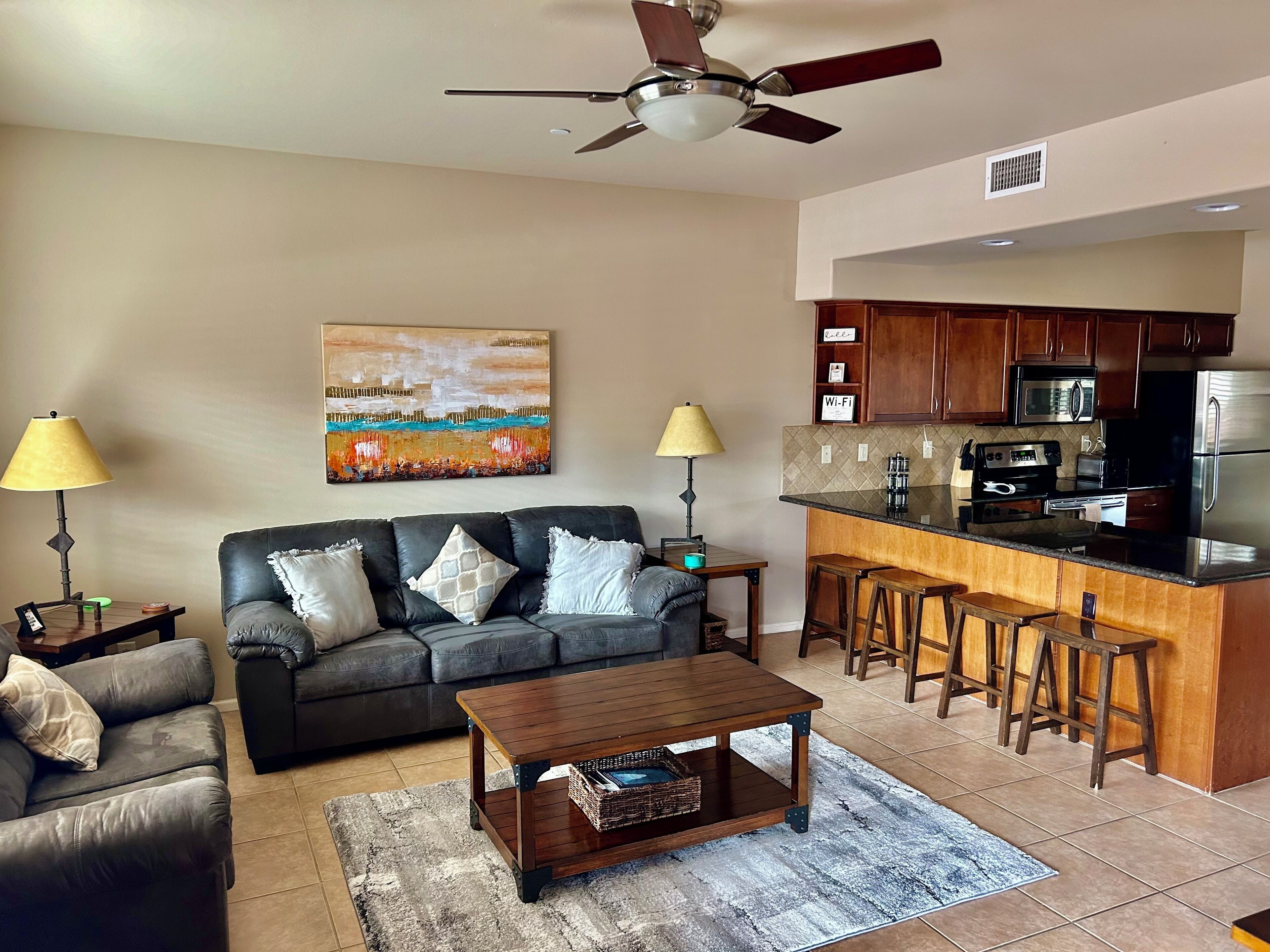 A living room with a sofa, coffee table, and a kitchen area with a bar and stools.