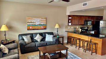 A living room with a sofa, coffee table, and a kitchen area with a bar and stools.