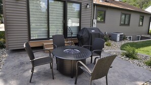 Une terrasse extérieure avec une table ronde, quatre chaises, un foyer et un barbecue.