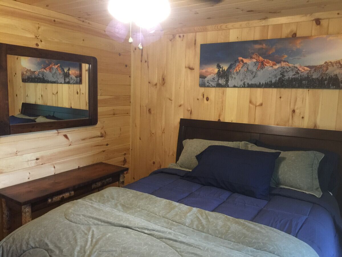 A wooden cabin room with a bed, a bench, and two paintings on the walls.