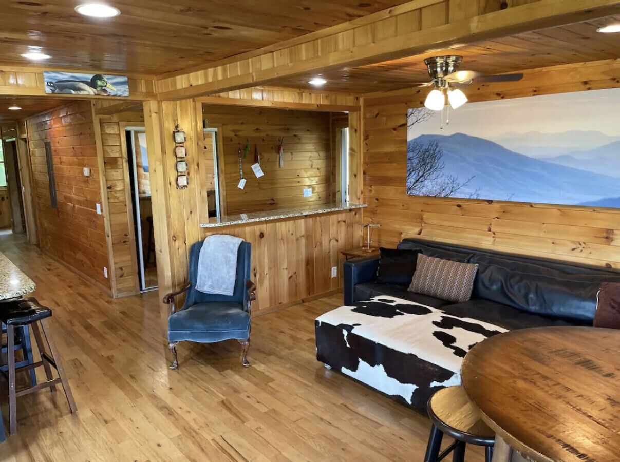 A wooden interior with a sofa, a chair, a bar area, and a painting of mountains.
