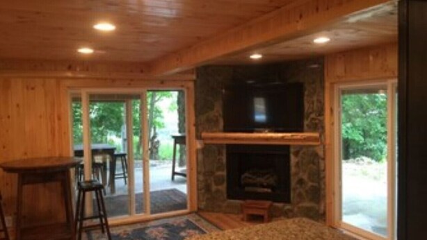 A wooden interior with a stone fireplace, a television above it, and a dining area with a table and chairs. - KastleRock Brand new 5 min to Slopes PoolTable Jacuzzi VIEWS PRIVATE sleep15 (Banner Elk)