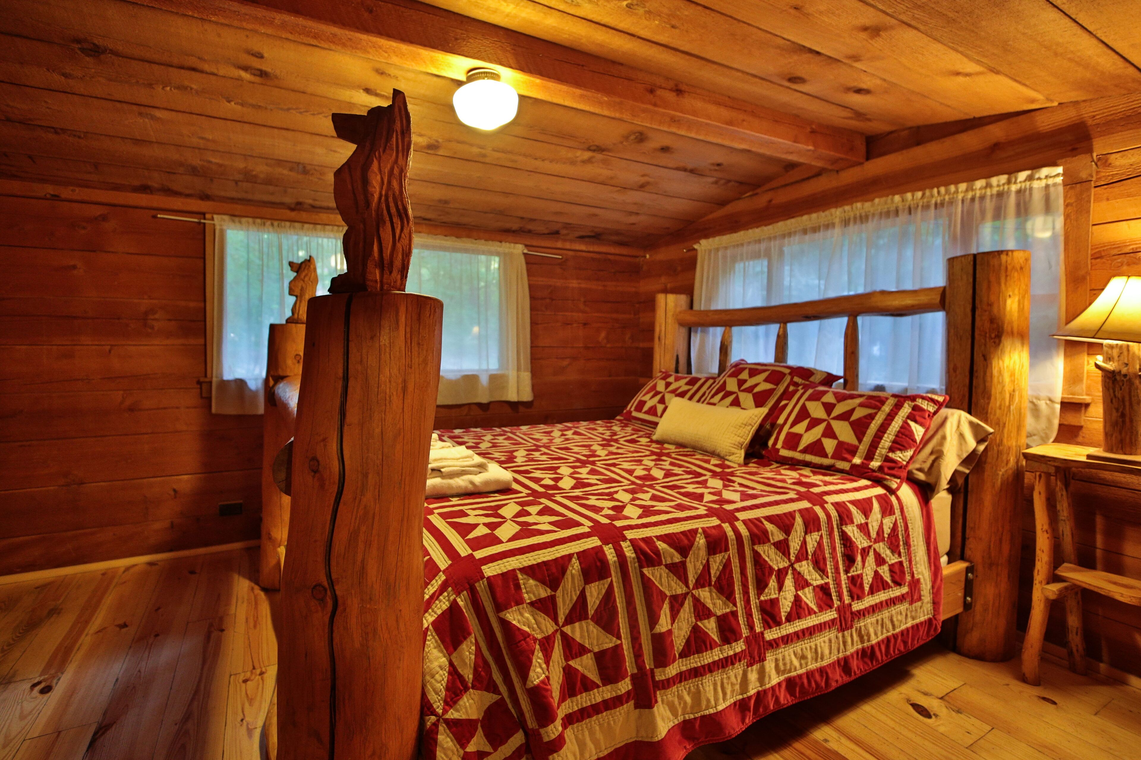 A wooden cabin bedroom with a bed, a nightstand, and a window with curtains.