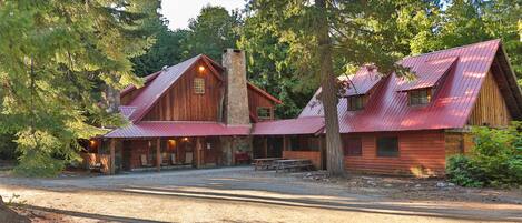 A rustic cabin with a stone chimney, wooden exterior, and a covered porch area.