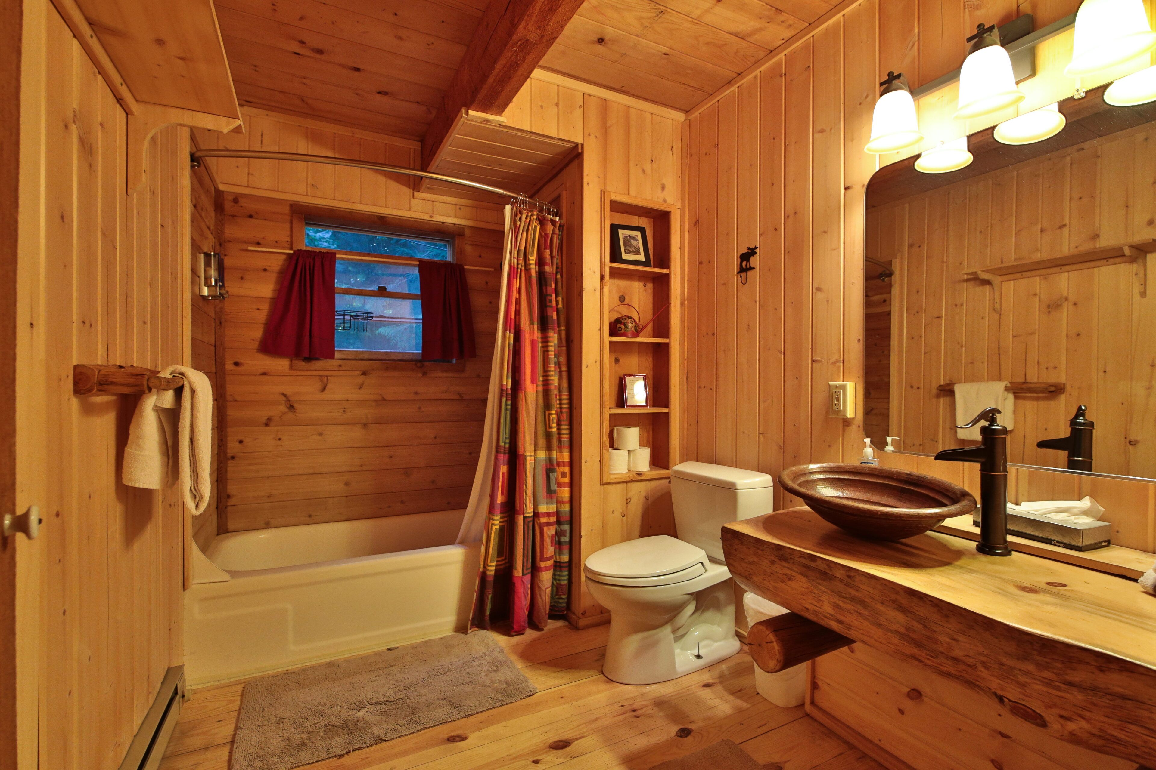 A wooden cabin bathroom with a bathtub, toilet, and wooden vanity.