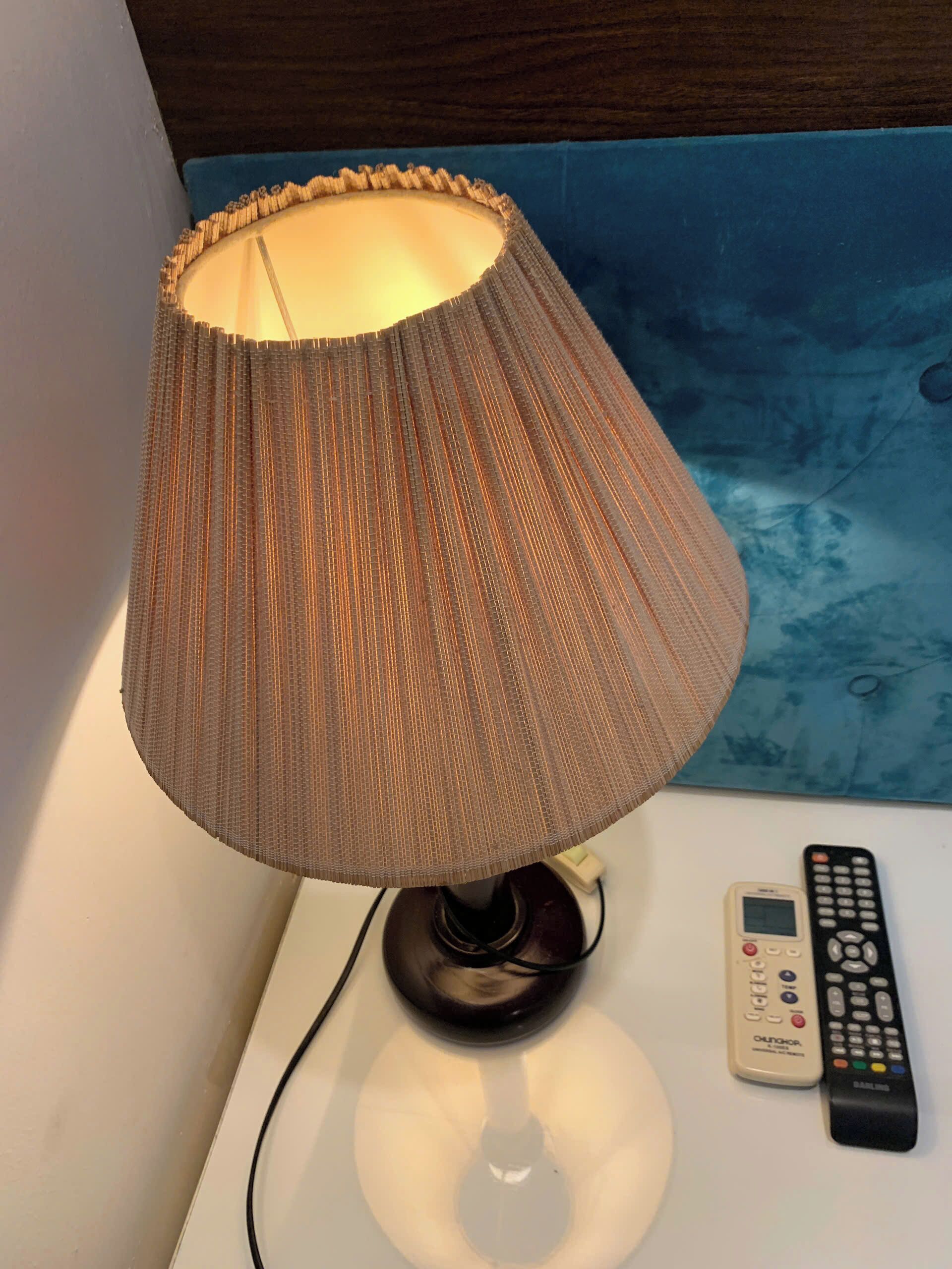 A lamp with a ribbed lampshade on a bedside table next to a remote control.