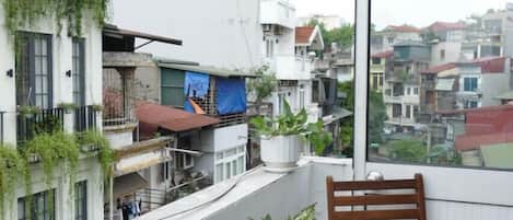A balcony with two wooden chairs and a potted plant, overlooking a densely packed urban area with various buildings.