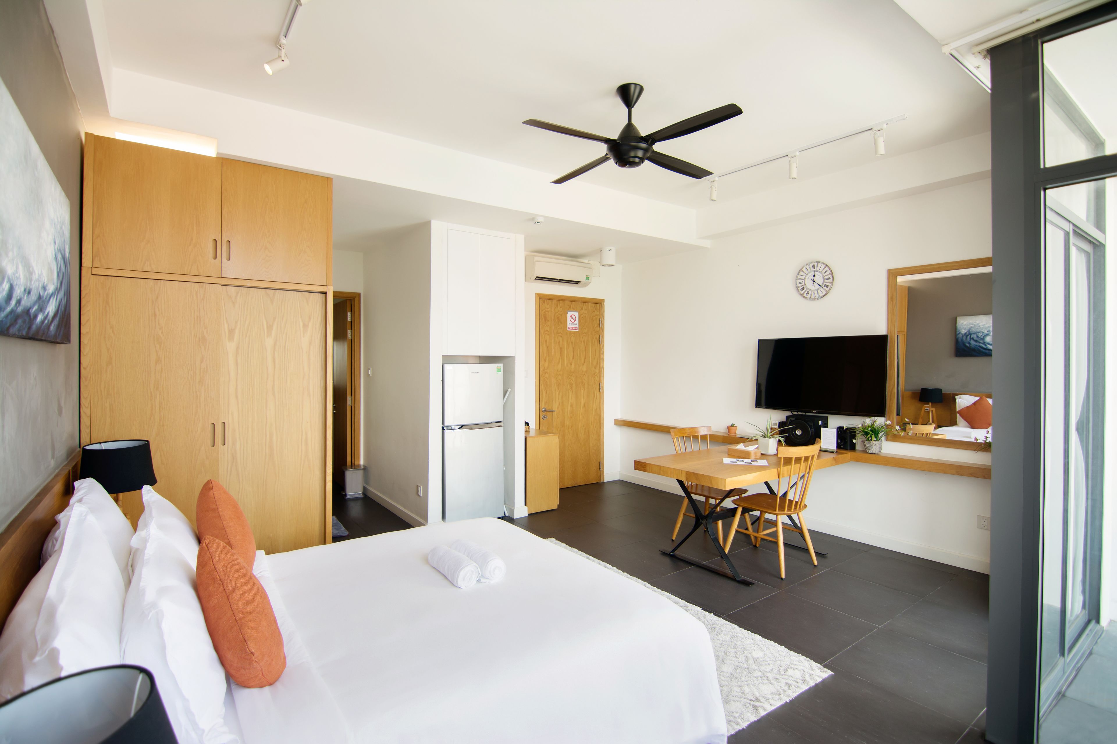 A hotel room with a bed, a desk, a chair, a television, and a ceiling fan.