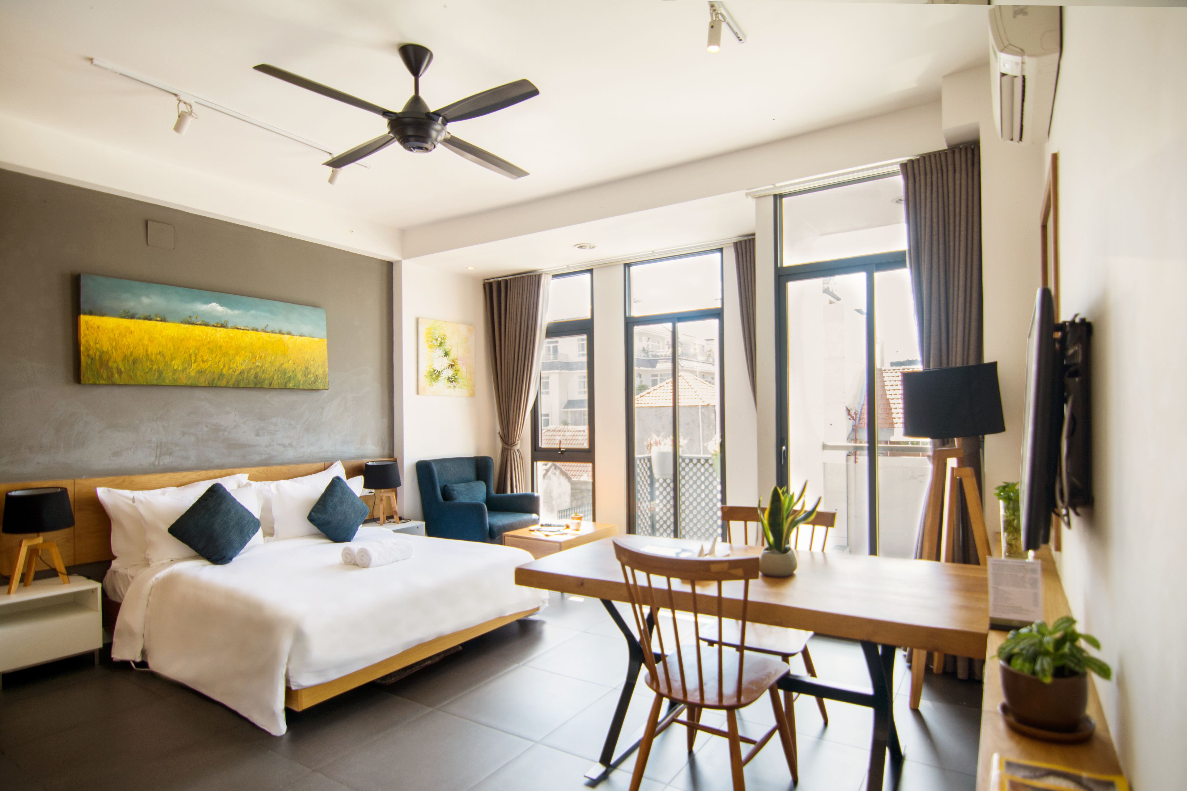Quarto de hotel moderno com cama grande, área de refeições e varanda com cortinas.