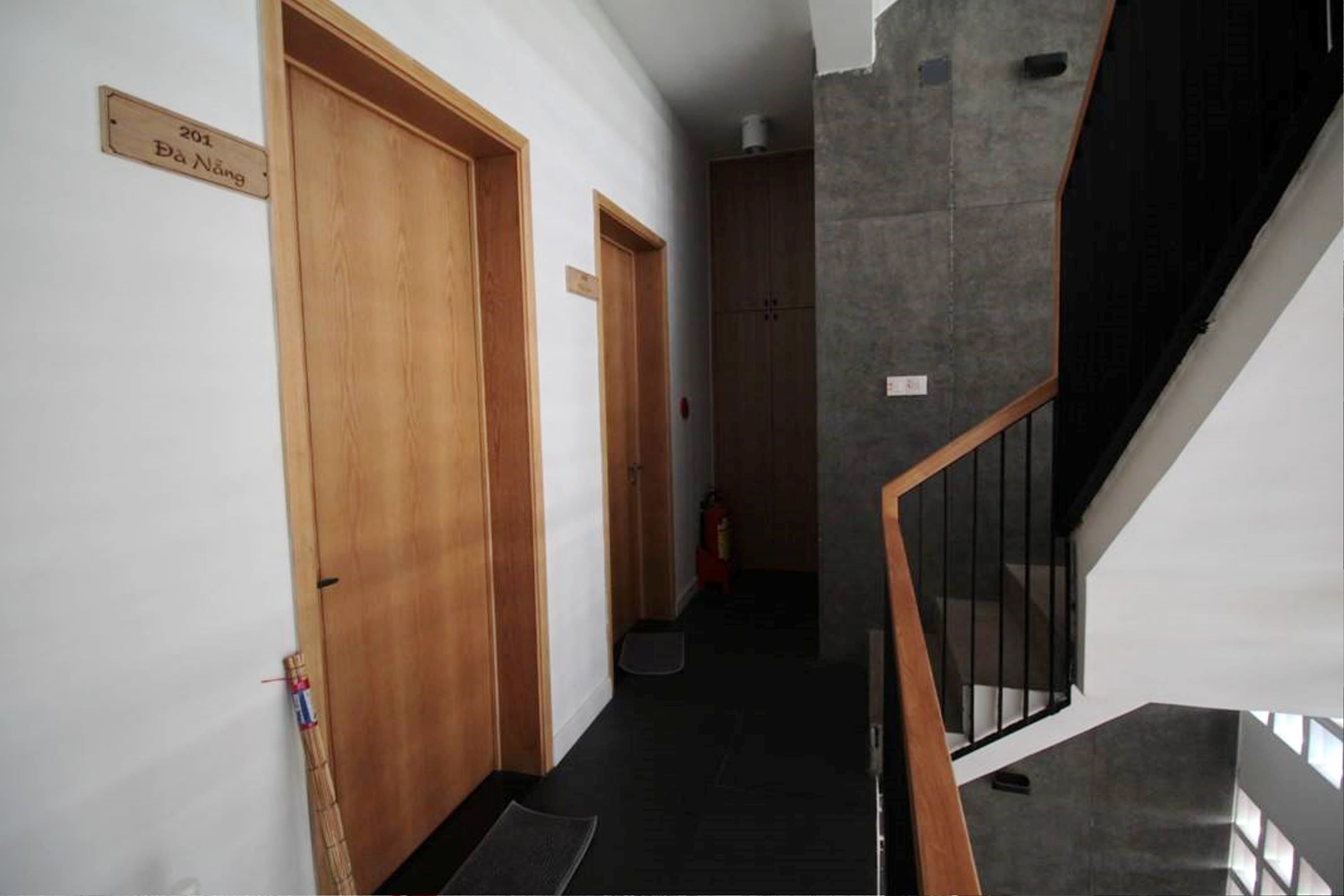 A hallway with wooden doors, a staircase with black railings, and a fire extinguisher on the floor.