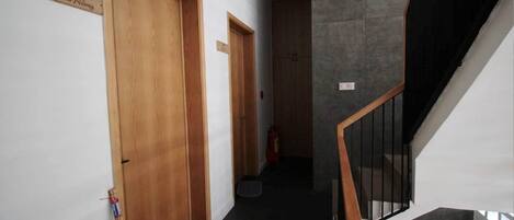 A hallway with wooden doors, a staircase with black railings, and a fire extinguisher on the floor.