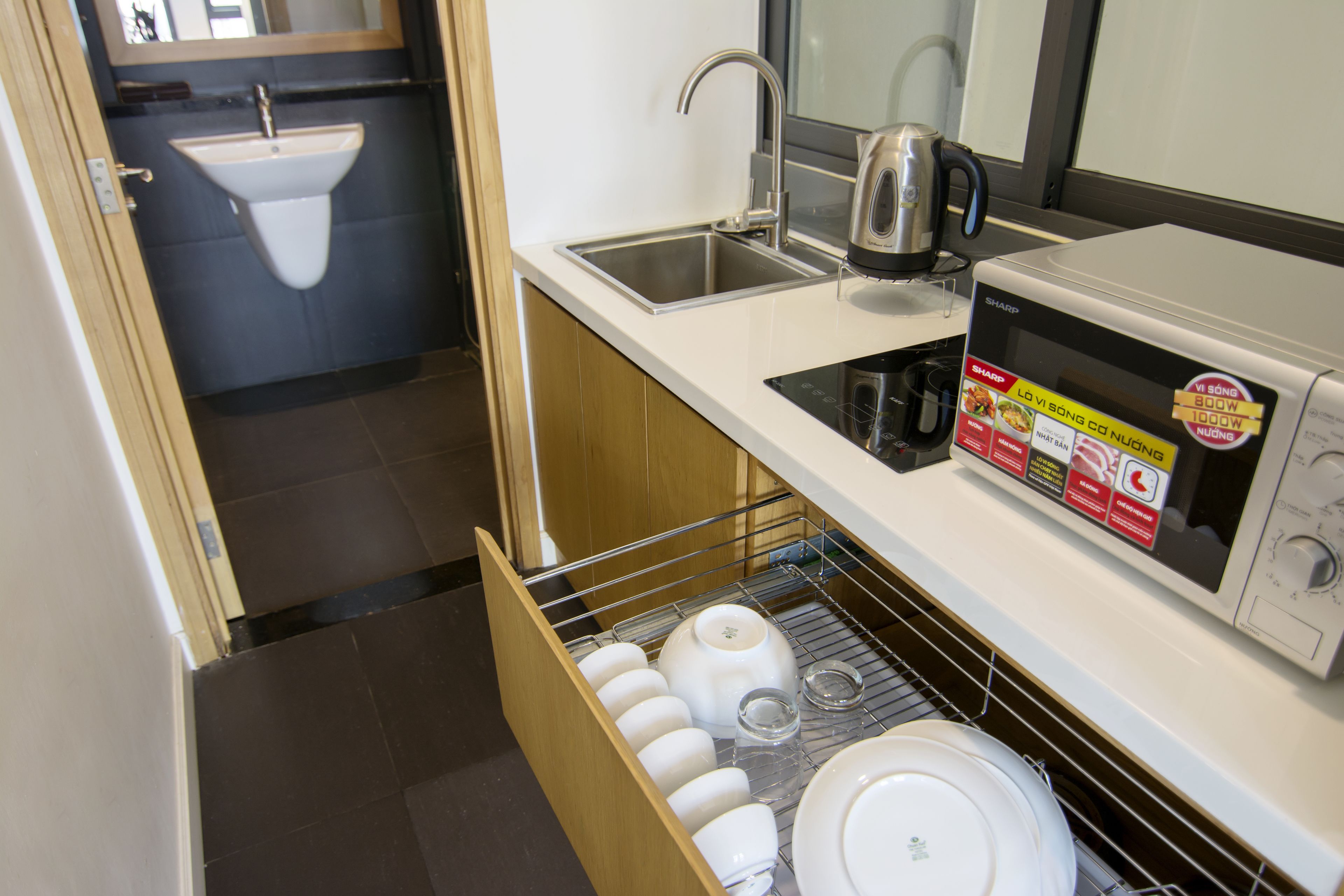 A compact kitchen with a sink, a kettle, a microwave, and a dish drying rack.
