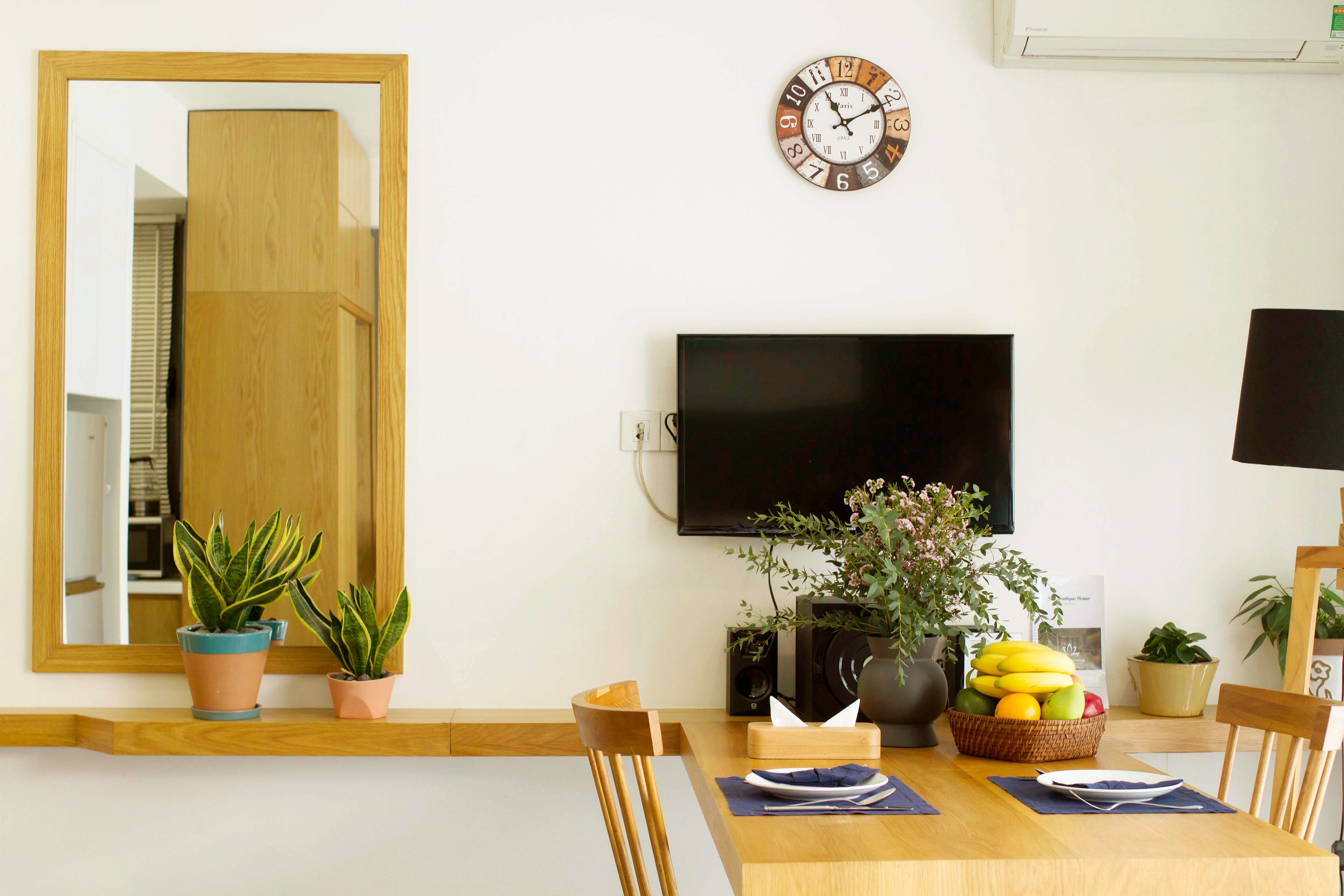 A dining area with a wooden table, chairs, a TV, and potted plants.