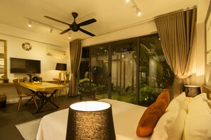 A hotel room with a bed, a desk, a chair, a TV, and a balcony with plants. - Sen Boutique House (Ho Chi Minh City)