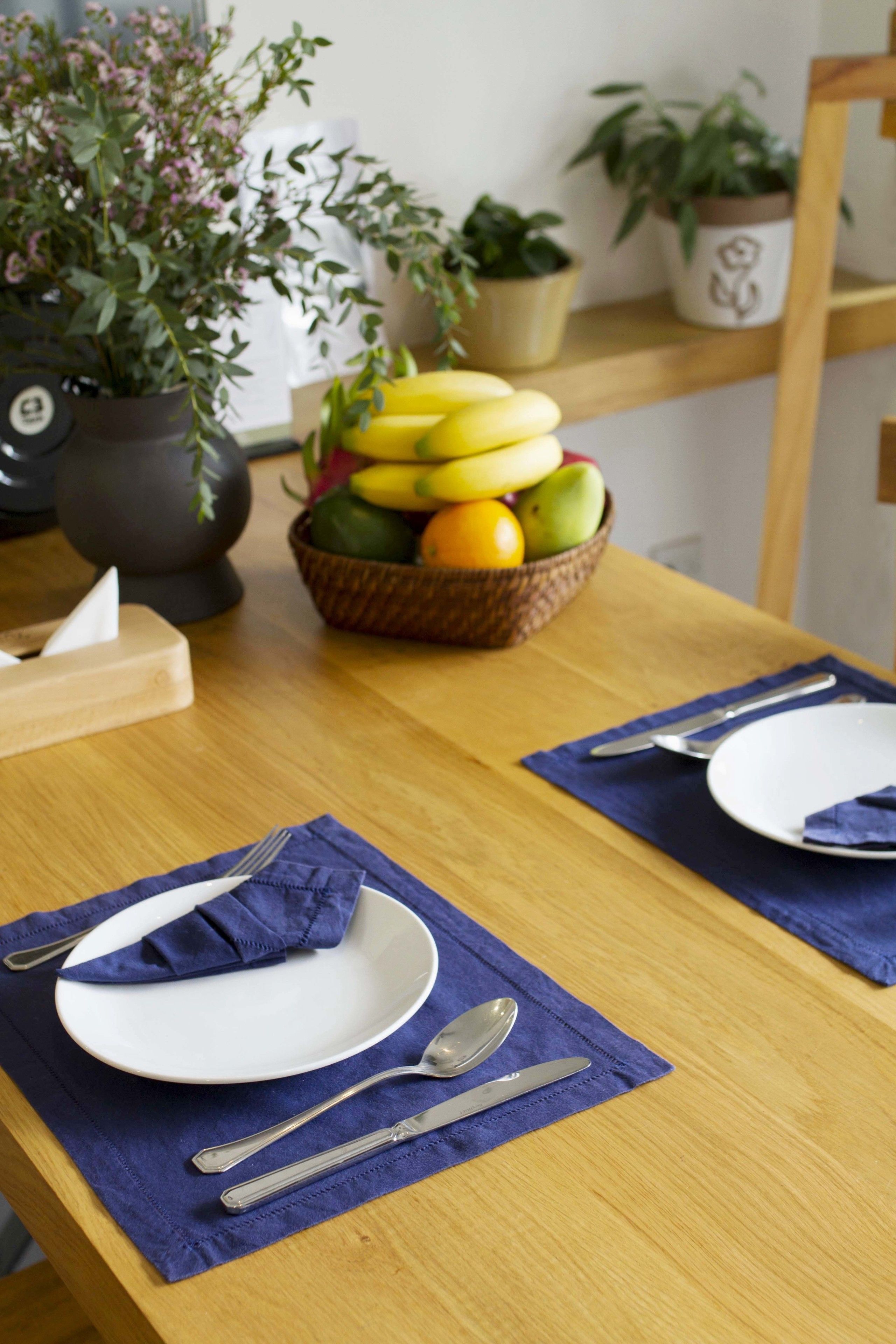 A dining table set with plates, cutlery, and a fruit bowl.