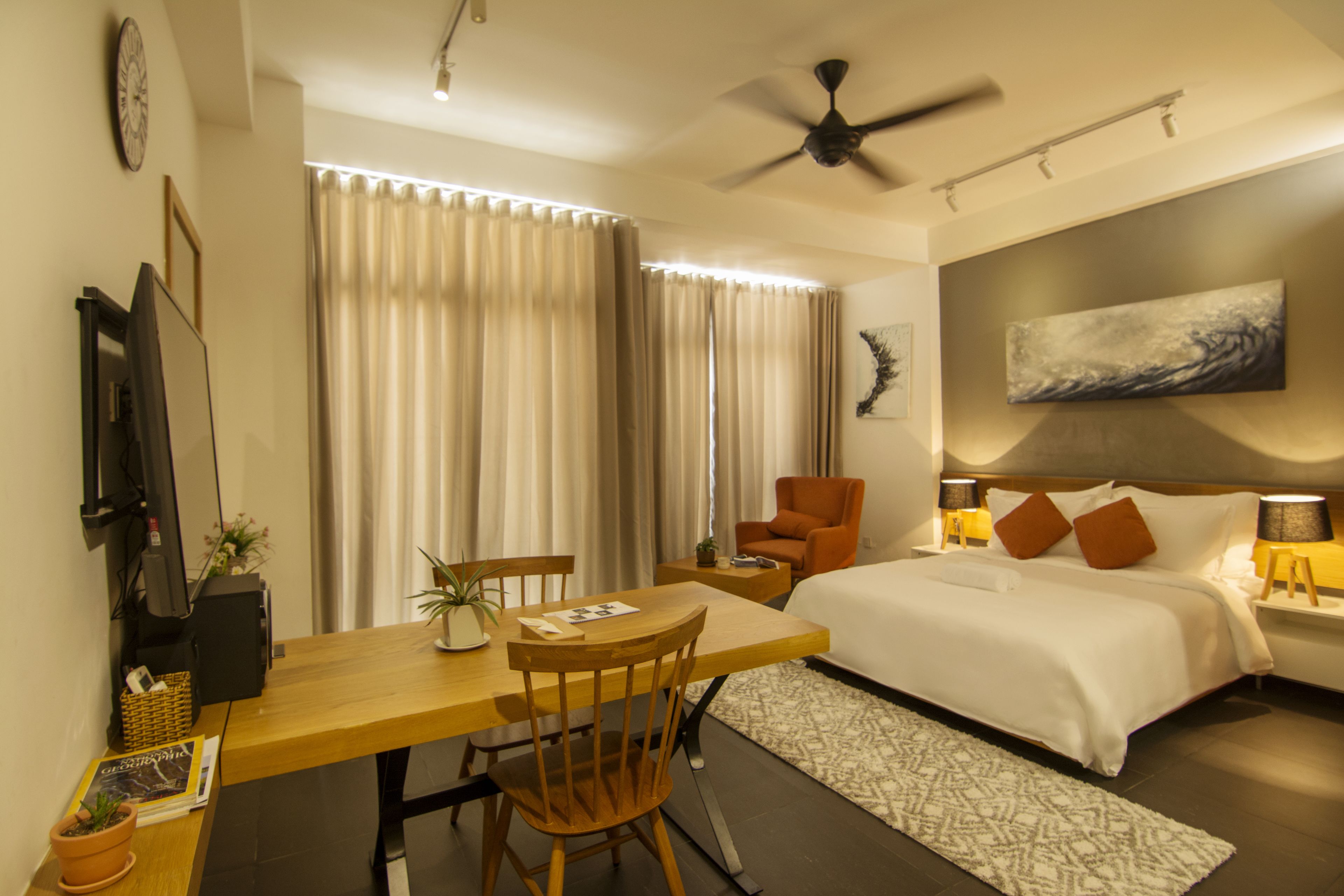 Una camera d'albergo moderna con un letto grande, una scrivania con sedia, un tavolo da pranzo e una ventola a soffitto.