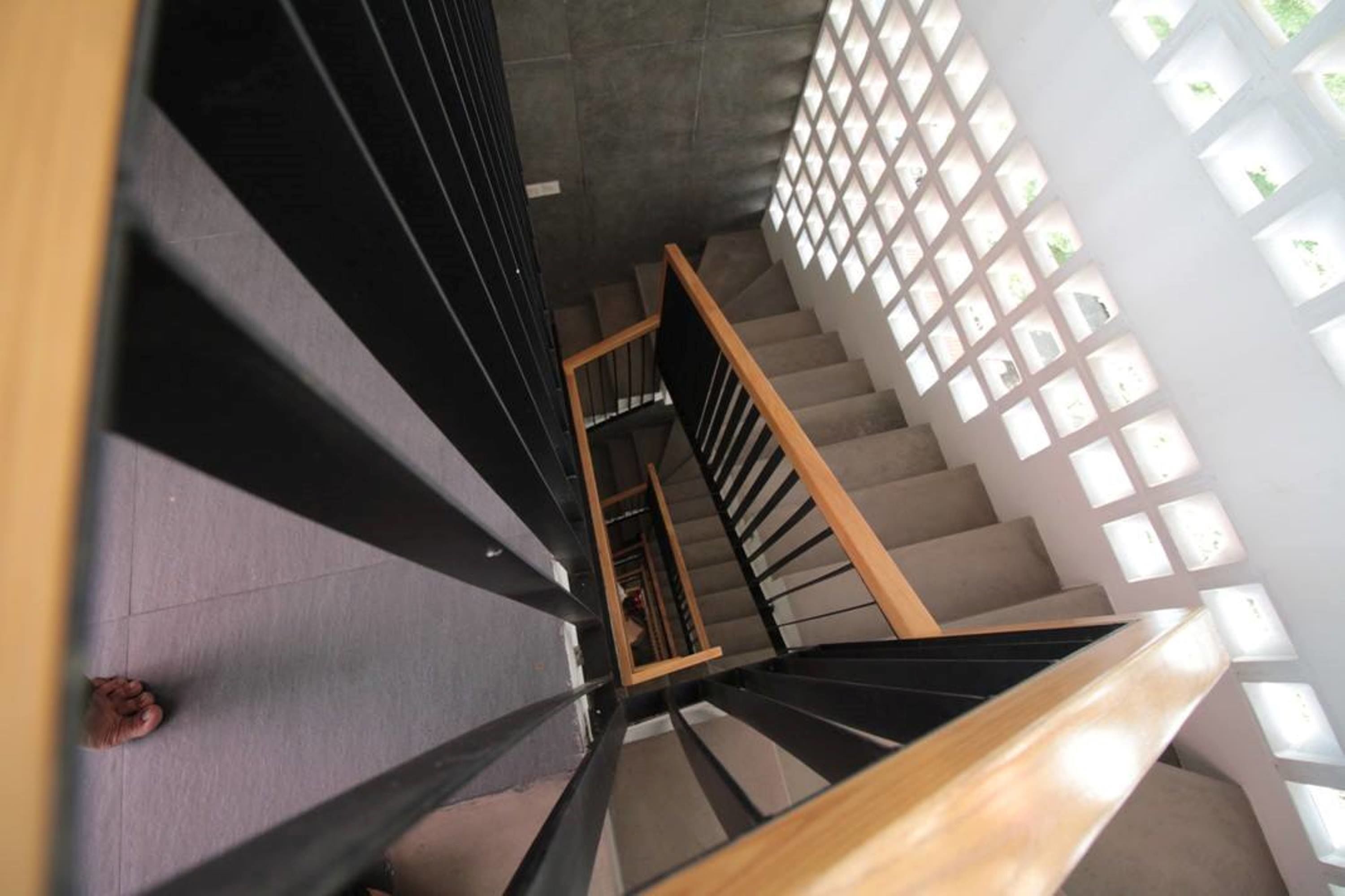 Un escalier en colimaçon doté d’une rampe en bois et de balustrades noires, menant à un palier d’où l’on peut admirer un mur blanc orné de fenêtres carrées.