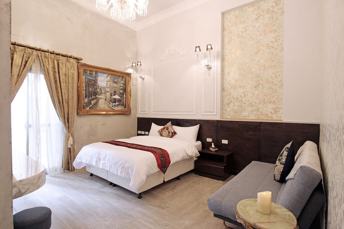 A hotel room with a large bed, a sofa, a small table with a candle, and a painting on the wall.