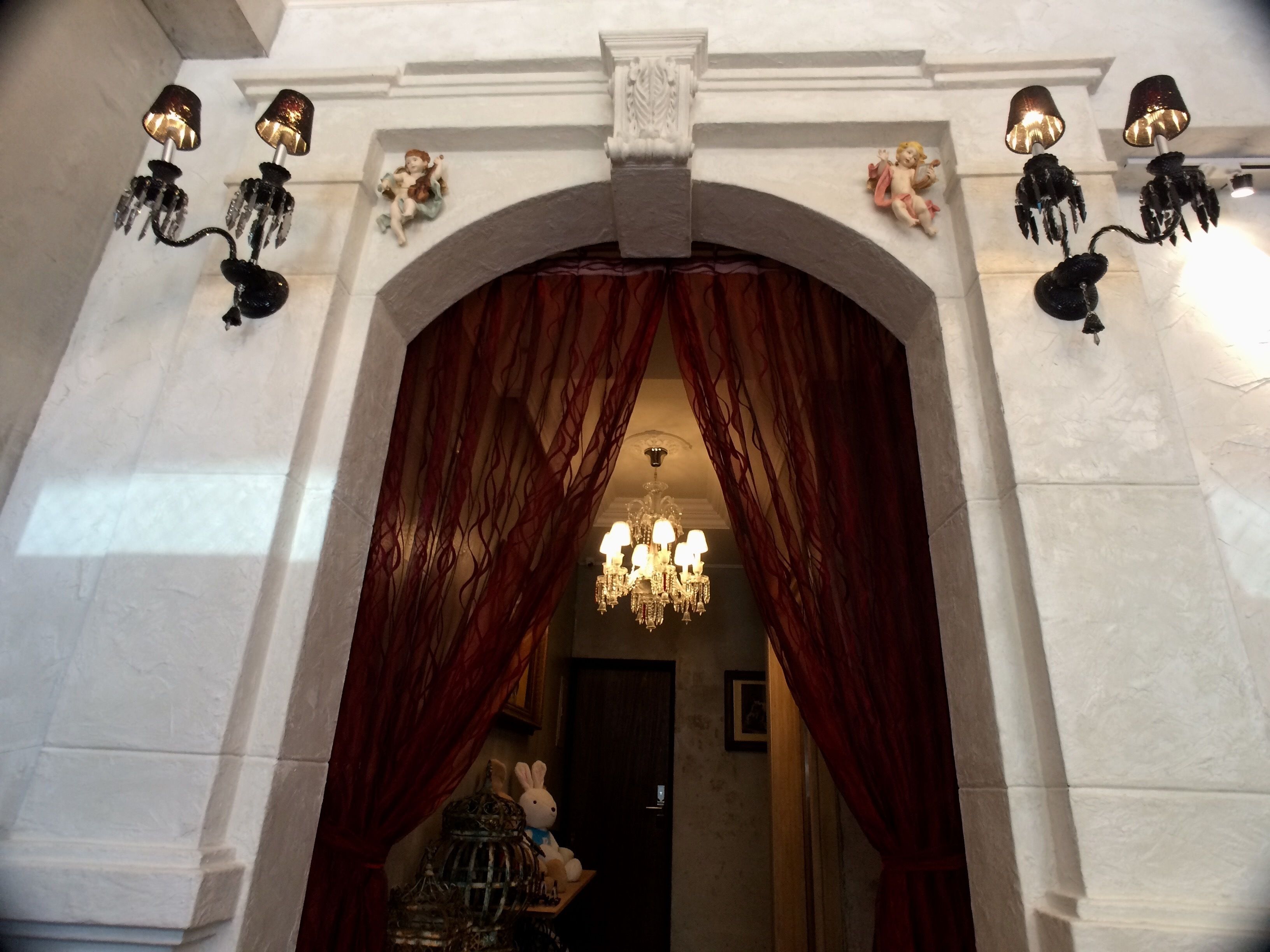 An arched doorway with red curtains, a chandelier, and wall-mounted sconces.