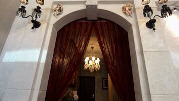 An arched doorway with red curtains, a chandelier, and wall-mounted sconces.