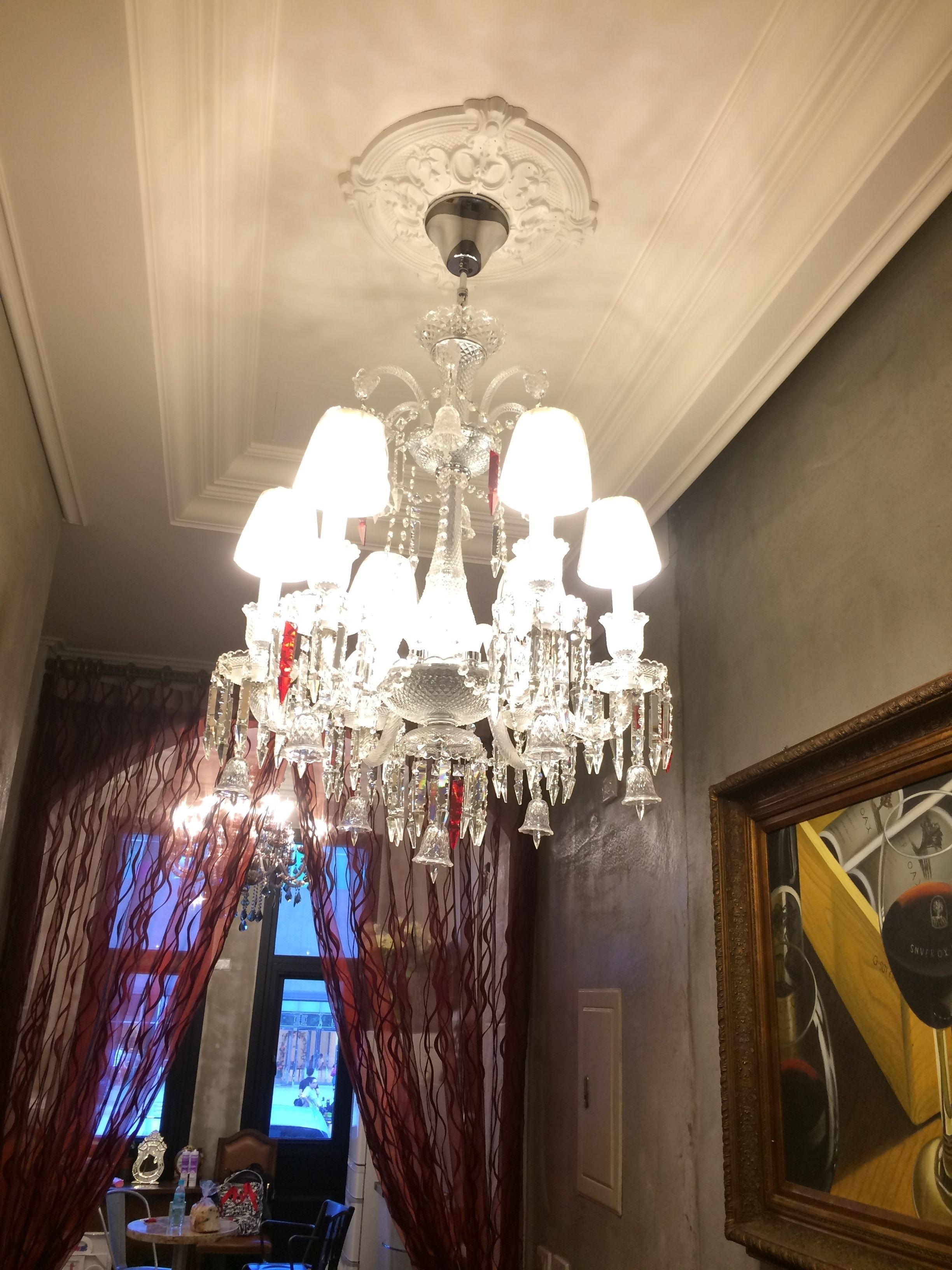 A chandelier with multiple arms and light fixtures, a framed artwork on the wall, and a table with items on it.