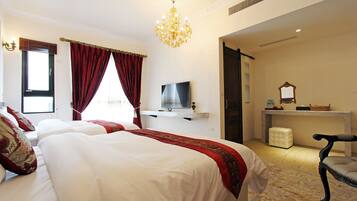 A hotel room with two beds, a TV, a desk, a chair, and a chandelier.