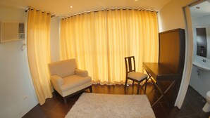 A living room with a sofa, a chair, a dining table, and a large window with yellow curtains. - Villa Del Rey Resort CamSur powered by Cocotel (Pili)