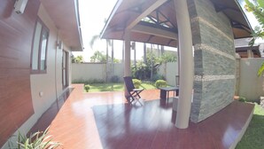 A covered patio area with a stone wall, a wooden deck, and a seating arrangement. - Villa Del Rey Resort CamSur powered by Cocotel (Pili)
