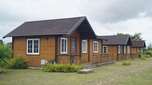 A row of wooden cabins with a sloped roof, a front porch, and a small garden area. - Villa Del Rey Resort CamSur powered by Cocotel (Pili)