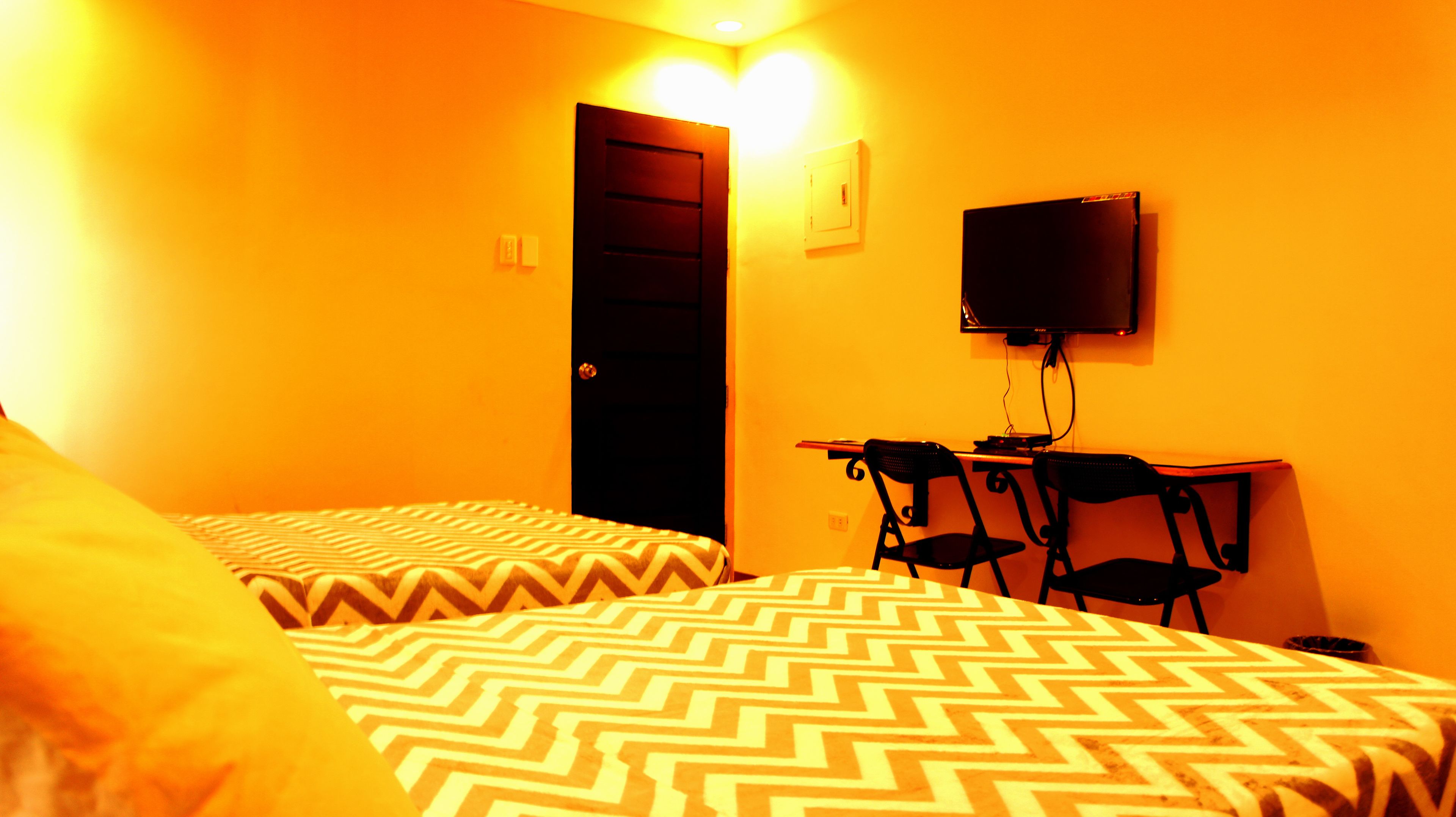 A room with two beds, a desk with chairs, a television, and a door.