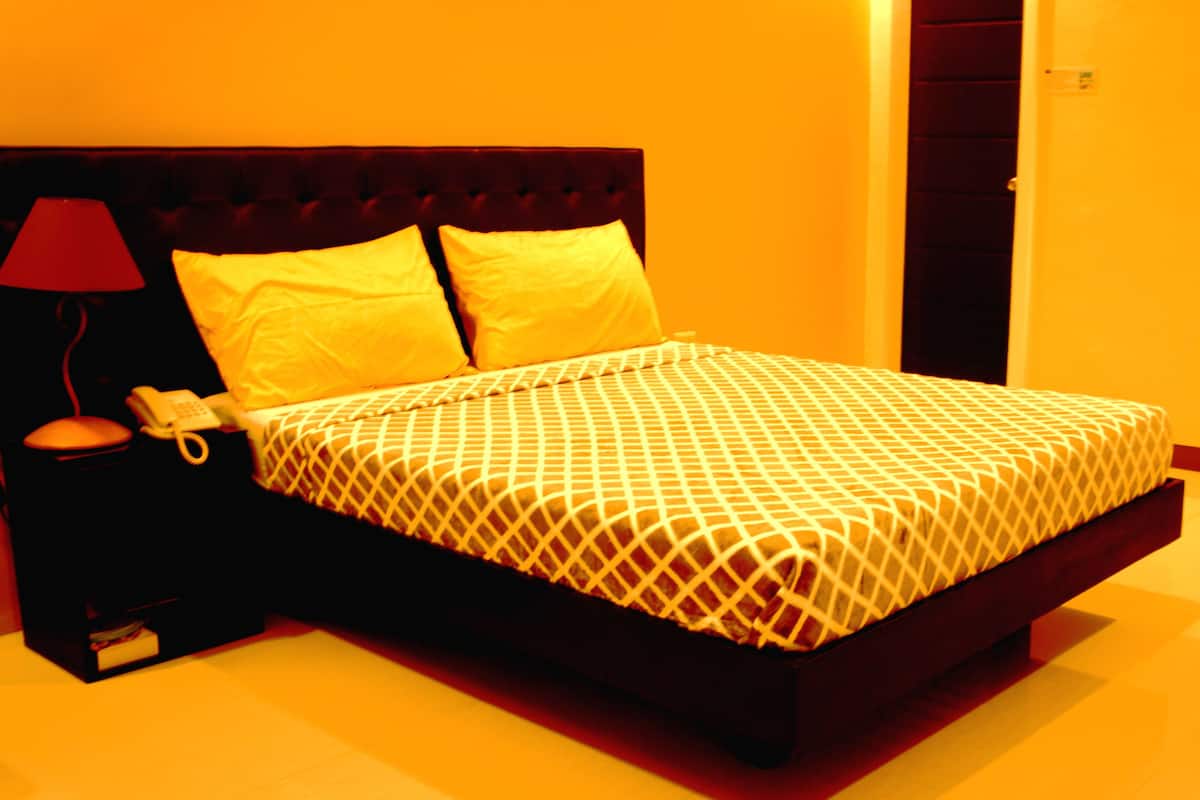 A neatly made bed with a patterned bedspread, a bedside lamp, and a telephone on a nightstand.