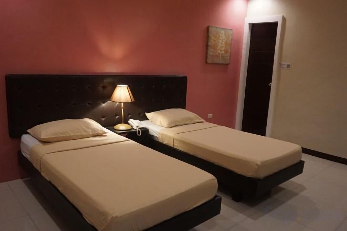 A hotel room with two single beds, a nightstand with a lamp, and a door to the right.
