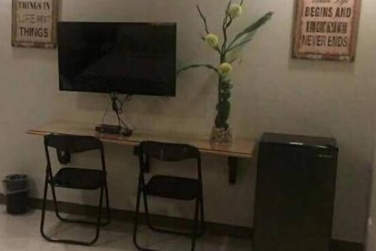 A small office with a desk, two chairs, a television, and a trash bin.
