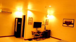 A room with a desk, two chairs, a flat-screen TV, an air conditioner, and two wall-mounted light fixtures. - Urbantel Hotel (Lucena)